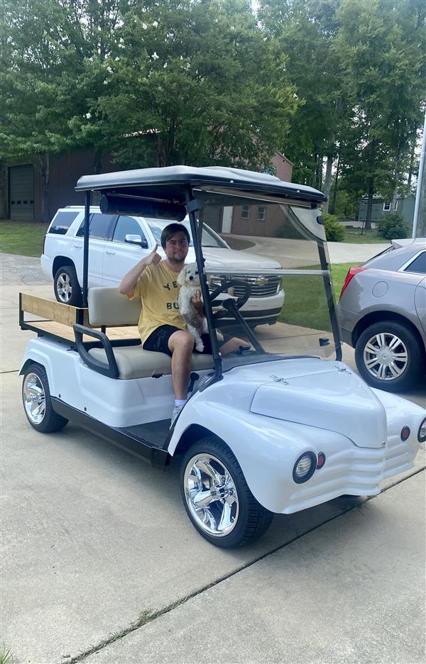 Peyton sits inside the golf cart and gives a thumbs up to the camera while holding a dog.